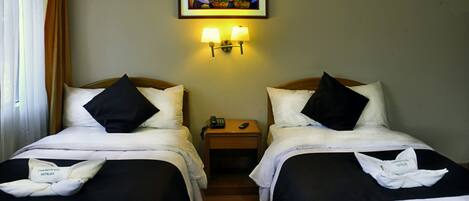 A hotel room with two beds, a nightstand, a painting on the wall, and a lamp.
