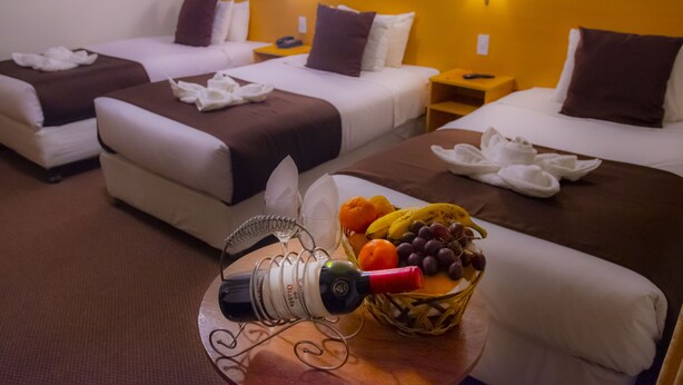 A hotel room with two beds, a fruit basket, a wine bottle, and a telephone on the nightstand.