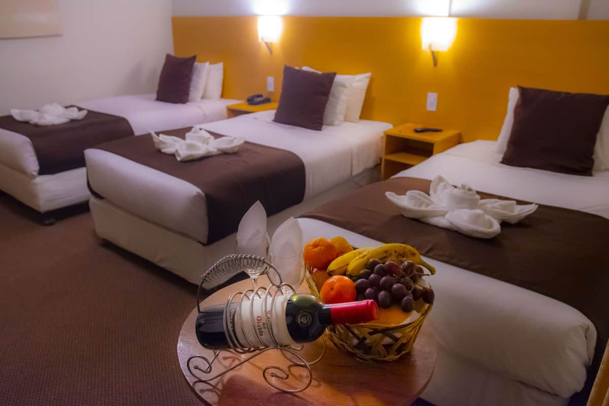 A hotel room with two beds, a bedside table with a phone, and a fruit basket on the floor.