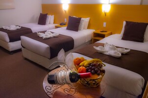 Habitación de hotel con dos camas, una cesta de frutas, una botella de vino y un teléfono en la mesita de noche.