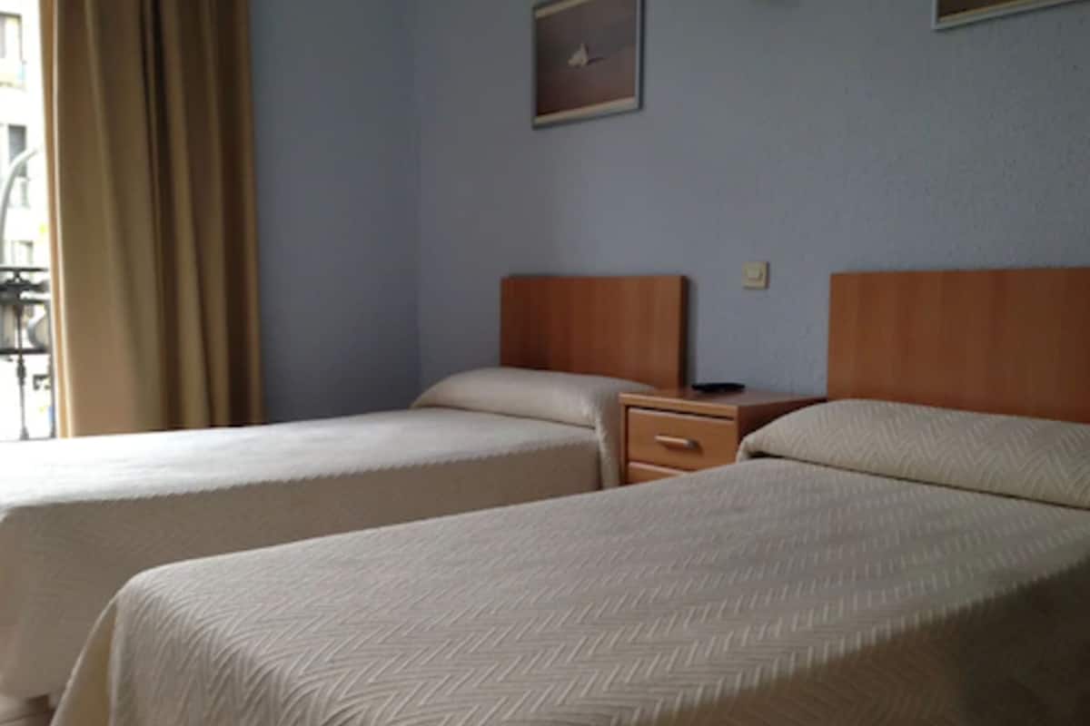 A hotel room with two beds, a wooden headboard, a nightstand, and a framed picture on the wall.