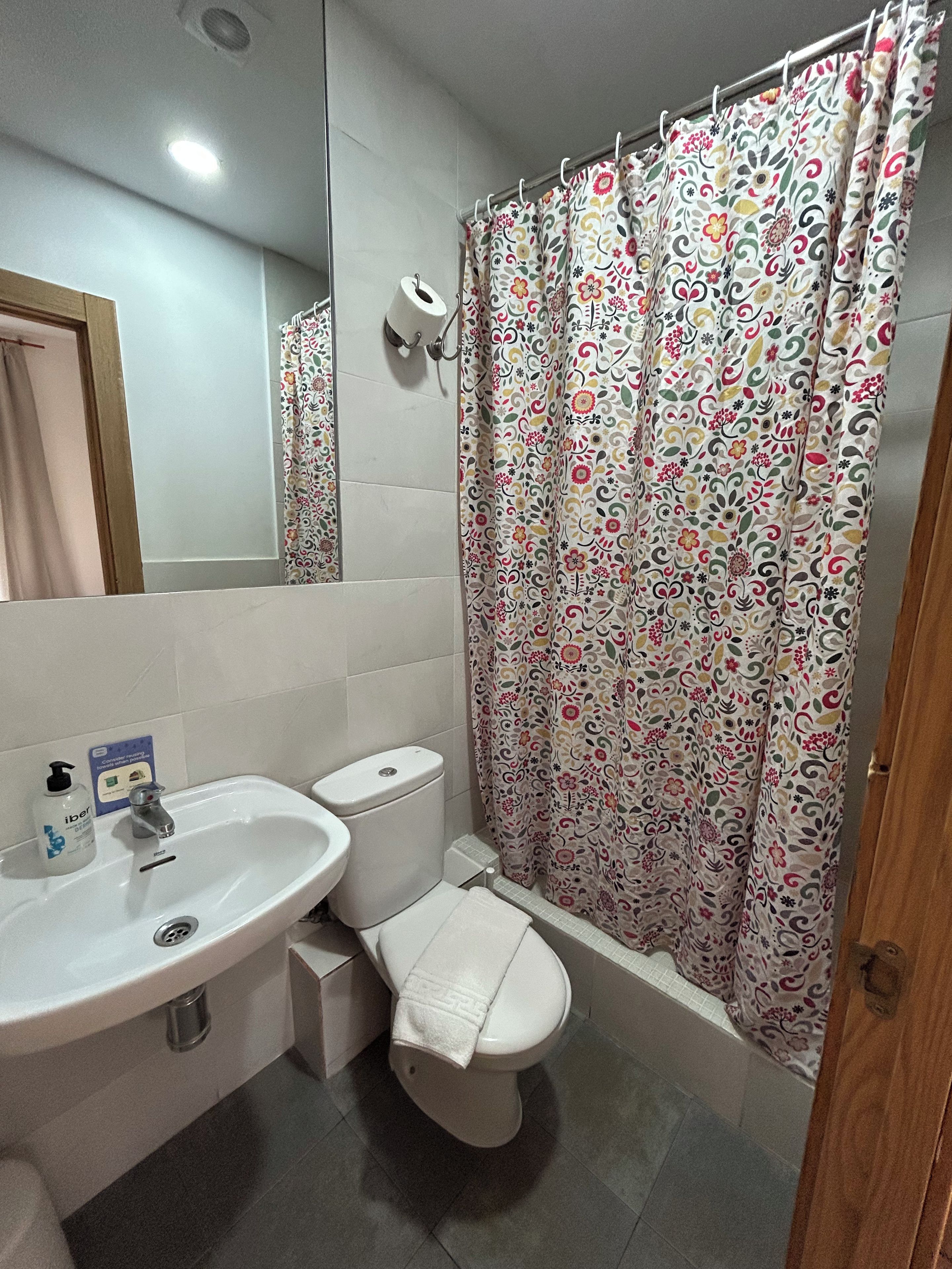 A bathroom with a white sink, toilet, and shower curtain with a floral pattern.