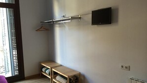 A room with a wooden bench, a TV mounted on the wall, and a radiator. - Hostal Delfos (Barcelona)