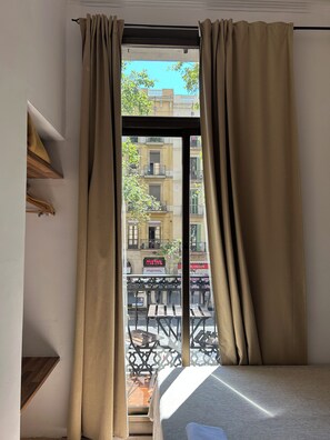 Una habitación con cama, ventana con cortinas y vista a la calle, con un letrero que dice 'MISTRAL'.