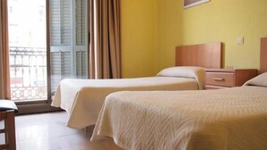 A hotel room with two beds, a wooden nightstand, a small table, and a window with curtains. - Hostal Delfos (Barcelona)