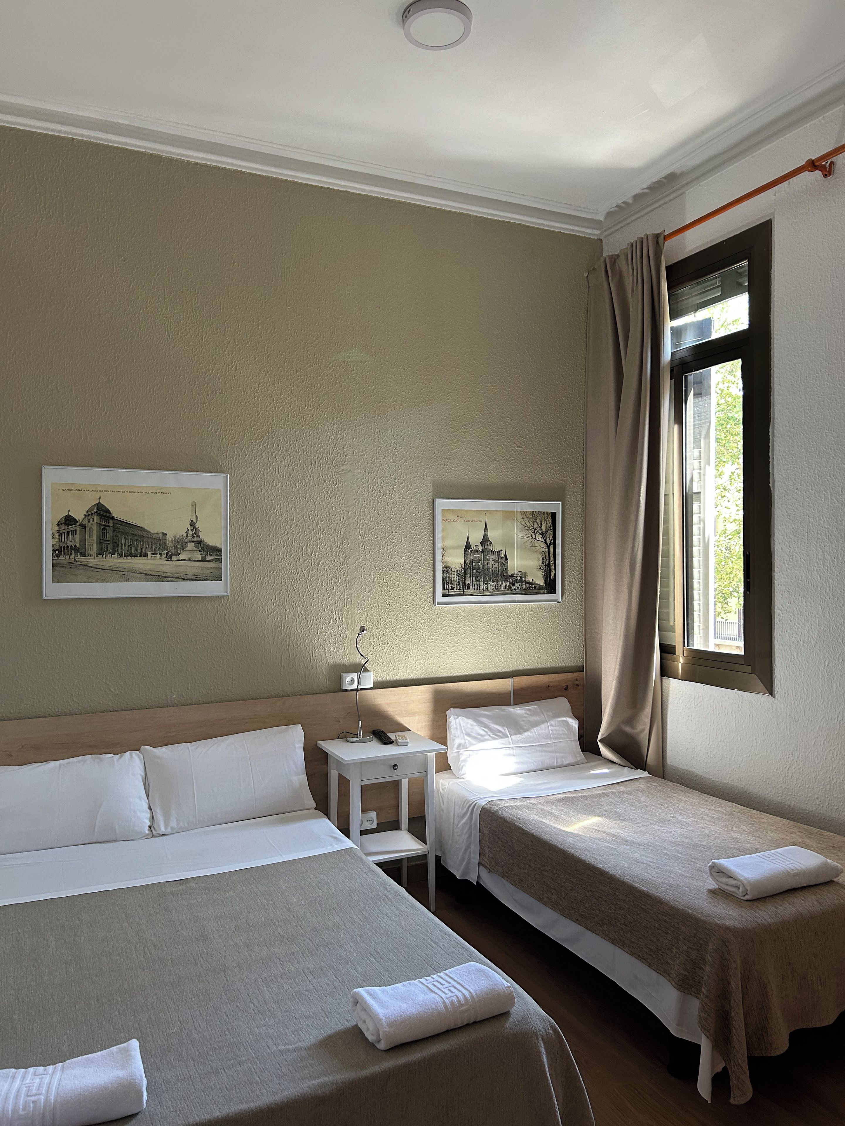 Una habitación de hotel con dos camas, una mesita de noche, una lámpara y dos cuadros en la pared.