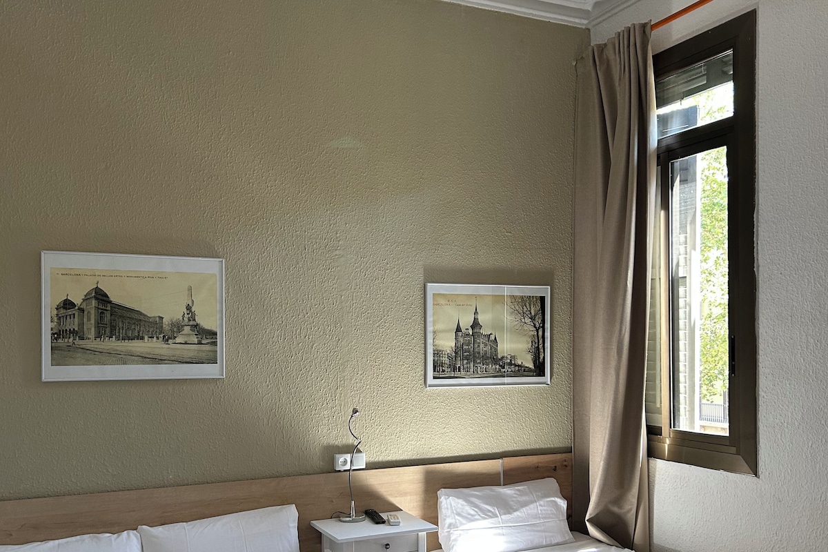 A hotel room with two beds, a nightstand, a lamp, and two framed pictures on the wall.