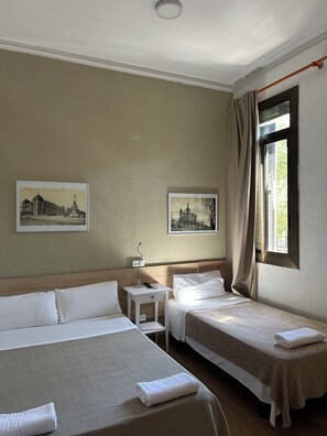Una habitación de hotel con dos camas, una mesita de noche, una lámpara y dos cuadros en la pared.