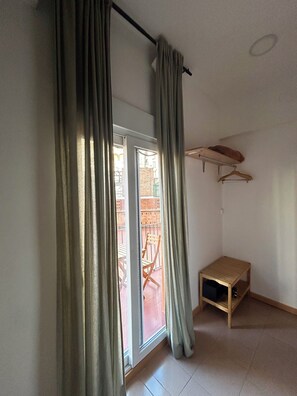 Quarto com porta de vidro deslizante, um pequeno banco de madeira e varal fixado na parede.