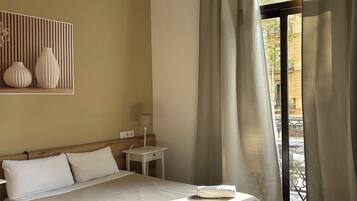 Habitación de hotel con cama, mesita de noche, lámpara y vistas a través de una ventana con cortinas.