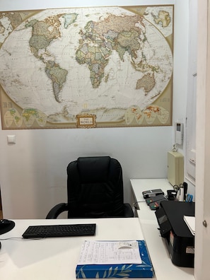 A room with a large world map on the wall, a desk with a computer, keyboard, and documents, and a black office chair. - Hostal Delfos (Barcelona)