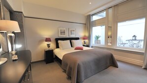 A hotel room with a bed, bedside lamps, a desk with a lamp, and a window with a view of the outside. - The Posthoorn (Amsterdam)