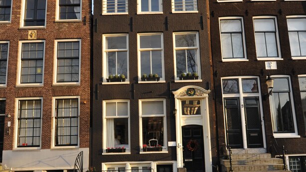 A row of traditional European townhouses with uniform brick facades, white window frames, and a central entrance with a decorative door. - The Posthoorn (Amsterdam)