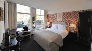 A hotel room with a large bed, a desk with a chair, a window with a view of the street, and a door. - The Posthoorn (Amsterdam)