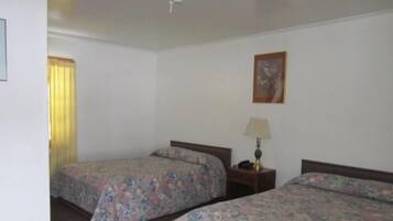 Une chambre avec deux lits, une table de chevet avec une lampe, un tableau encadré au mur et une fenêtre avec des rideaux.