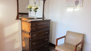 A wooden dresser with drawers and a mirror above it, a chair with a cushion, and a framed picture on the wall. - Cadet Motel (Cornwall)