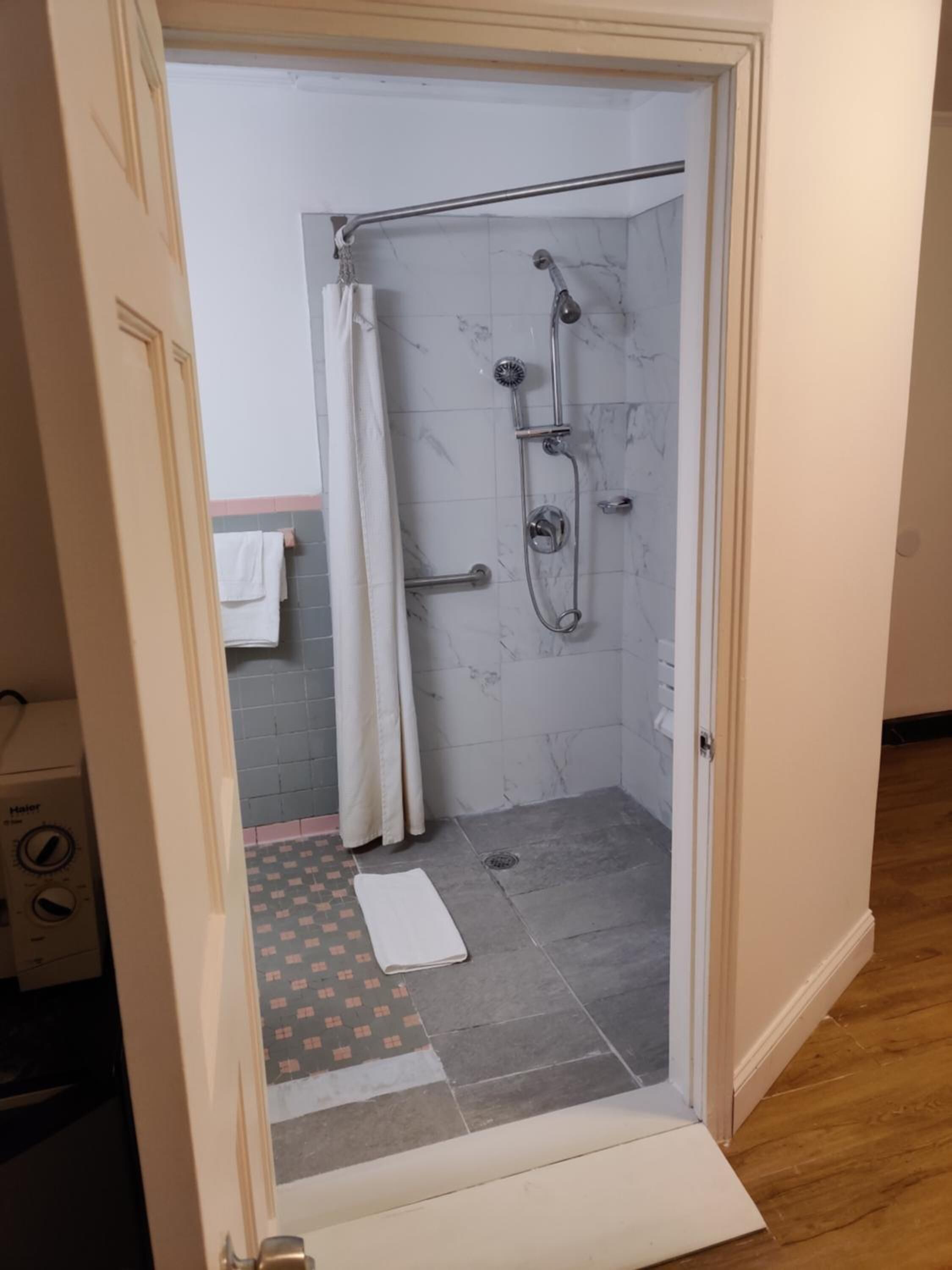 Una ducha a nivel con puerta de cristal, un perchero y un tapete estampado en el suelo.