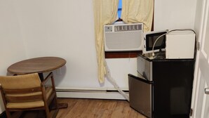 A compact room with a wooden floor, a small round table, a wooden chair, a white air conditioning unit, and a white refrigerator. - Cadet Motel (Cornwall)