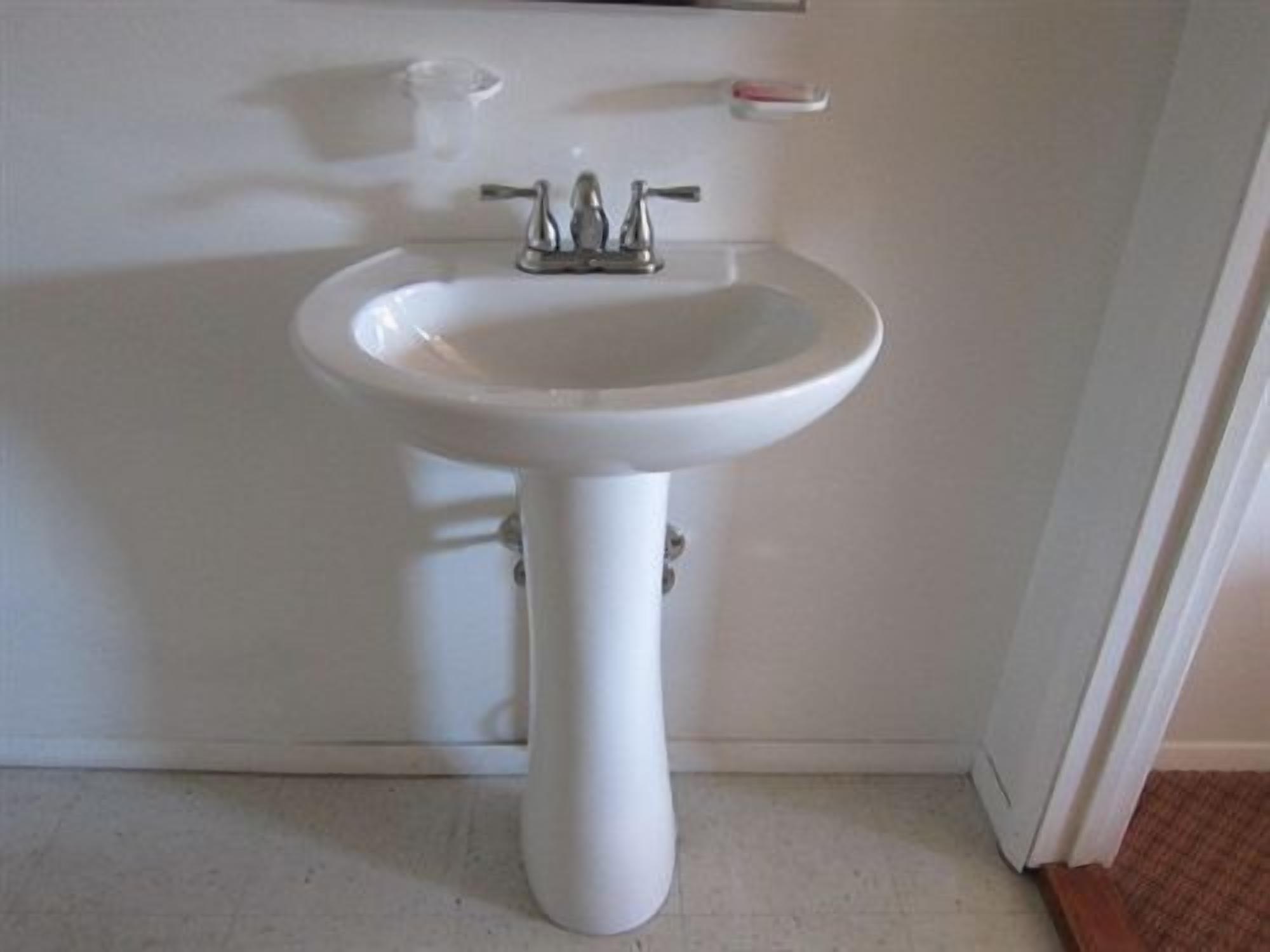 Un lavabo sur pied, de couleur blanche, doté d’un seul robinet et d’un porte-savon placé au-dessus.