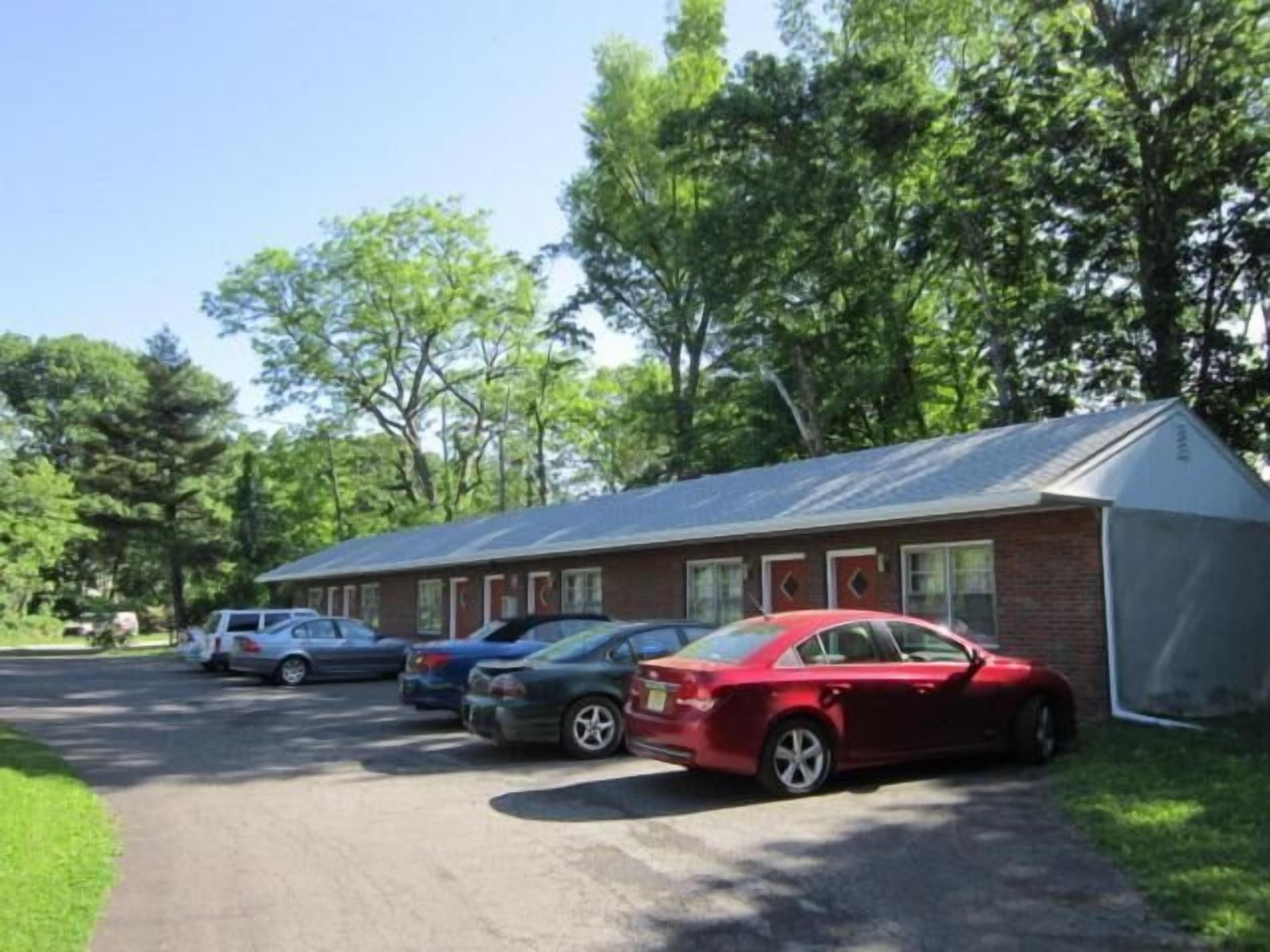 Ein Motel mit Backsteinfassade, überdachtem Parkplatz und Rasenfläche.