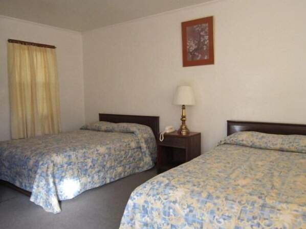 A hotel room with two beds, a bedside table with a lamp, a telephone, and a framed picture on the wall.