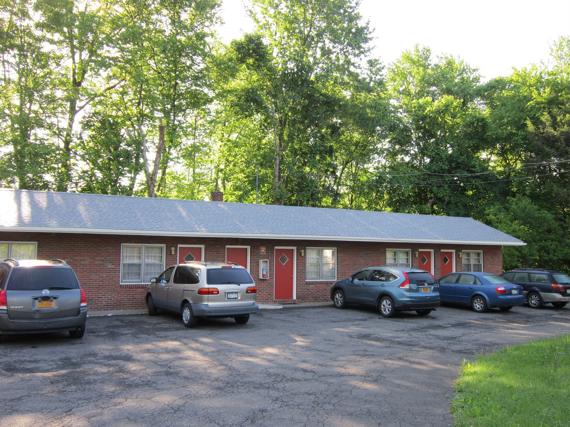 A motel with a brick exterior, multiple rooms with red doors, and a parking lot with several cars.