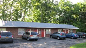 A motel with a brick exterior, multiple rooms with red doors, and a parking lot with several cars.