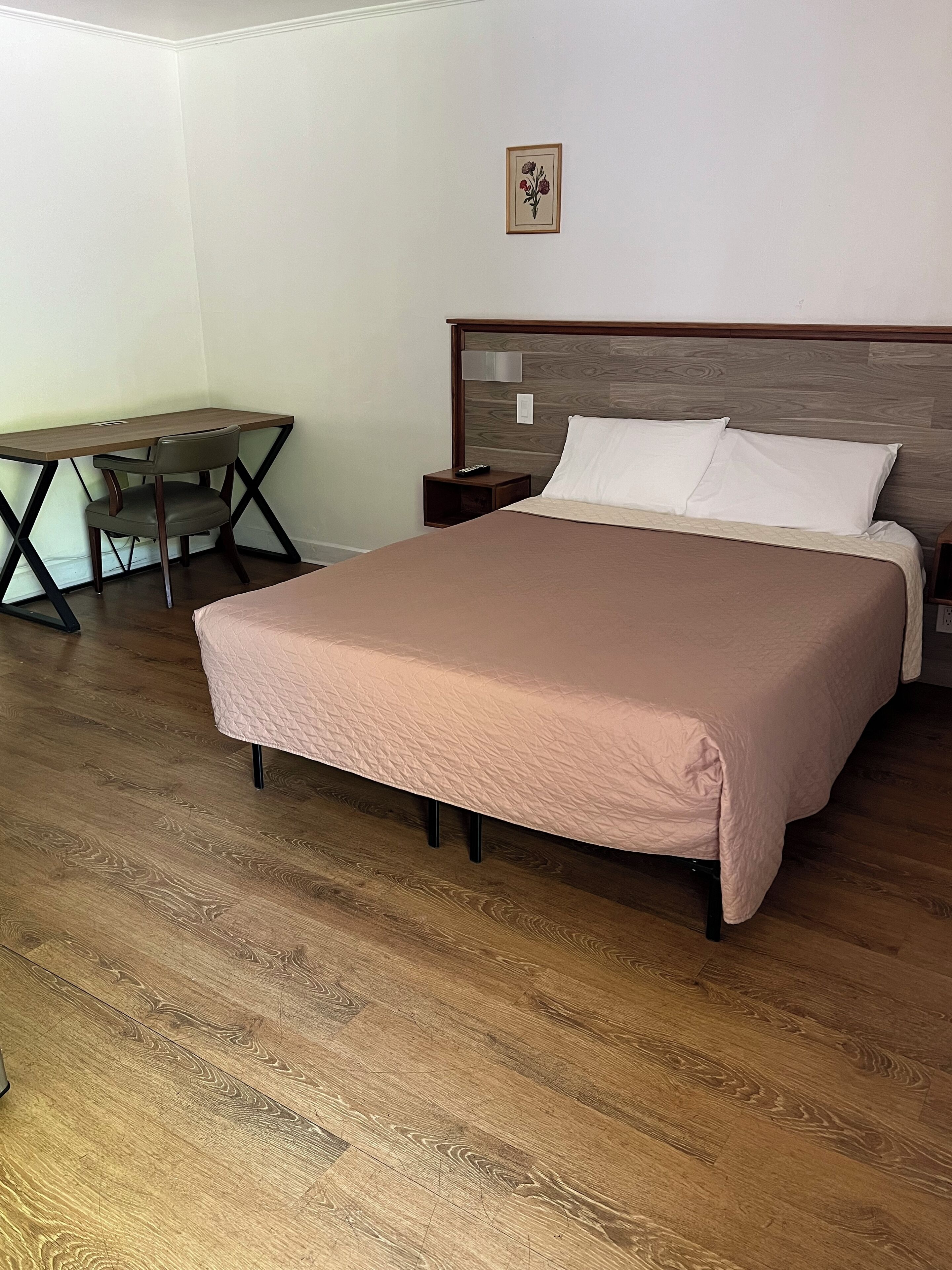 A bedroom with a bed, bedside table, nightstand, desk, and chair.