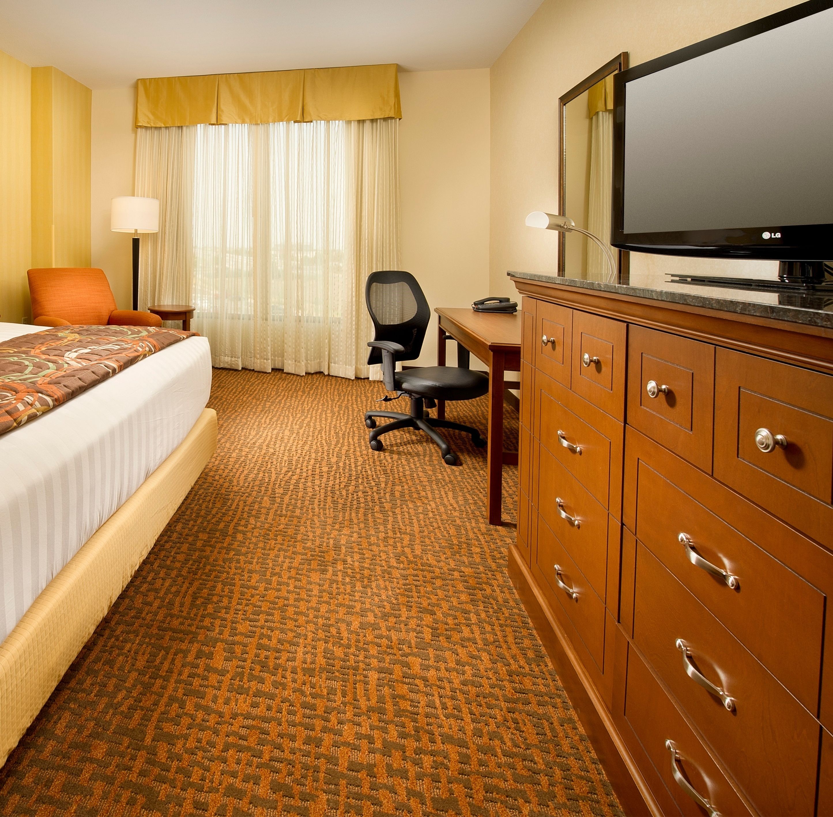 Une chambre d’hôtel comprenant un lit, un bureau, une chaise, une télévision et une commode.