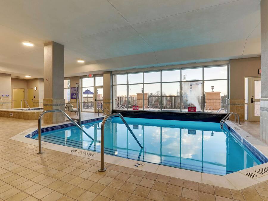 An indoor swimming pool with clear safety markings, a tiled floor, and large windows offering a view of the outside.