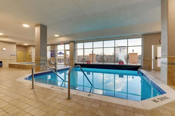 Una piscina interior con marcas de seguridad claras, suelo de baldosas y grandes ventanales que ofrecen vistas al exterior.
