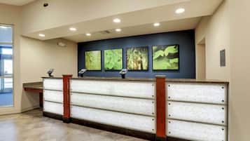 A reception desk with a modern design, featuring a marble-like surface and wooden accents. There are four framed botanical prints on the wall above the desk.