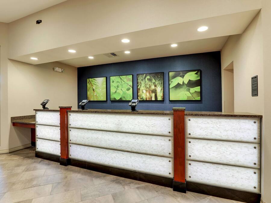A reception desk with a modern design, featuring a marble-like surface and wooden accents. There are four framed botanical prints on the wall above the desk.