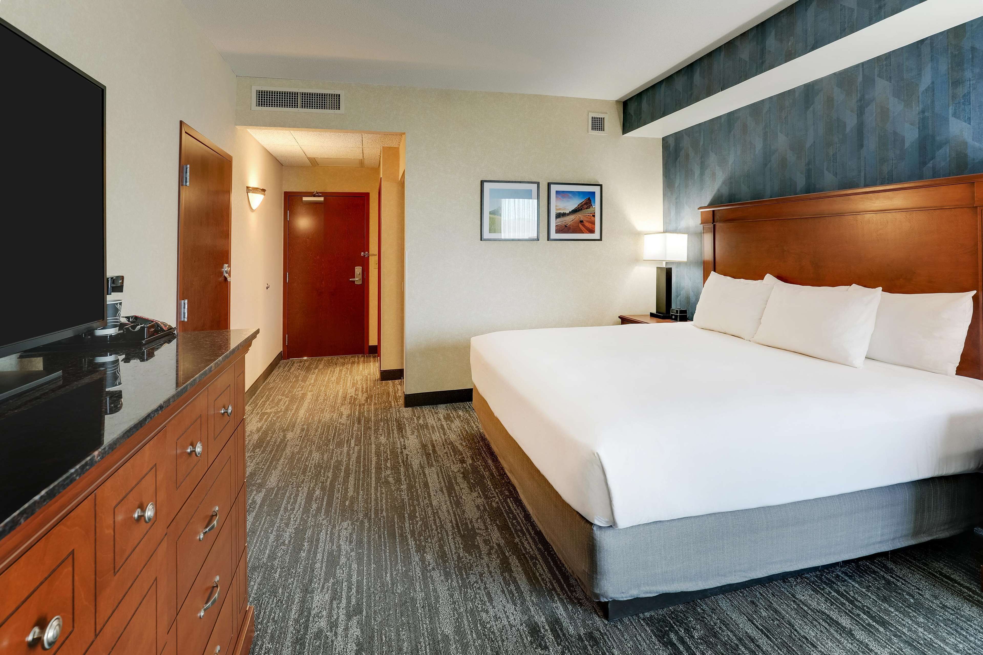 A hotel room with a large bed, a wooden dresser, a TV, and a door leading to another room.