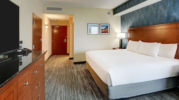 A hotel room with a large bed, a wooden dresser, a TV, and a door leading to another room.