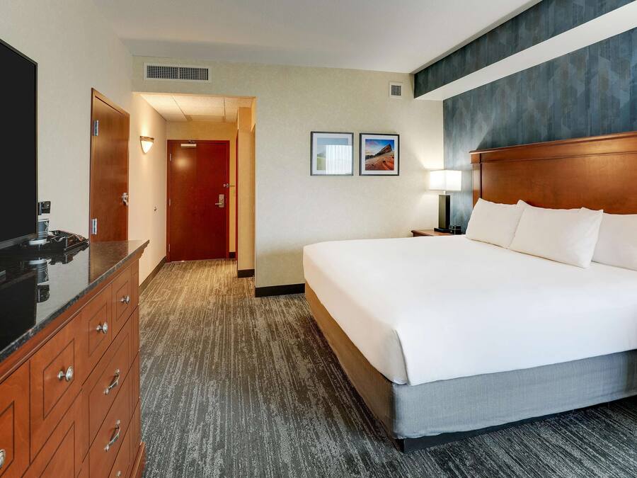 A hotel room with a large bed, a wooden dresser, a TV, and a door leading to another room.