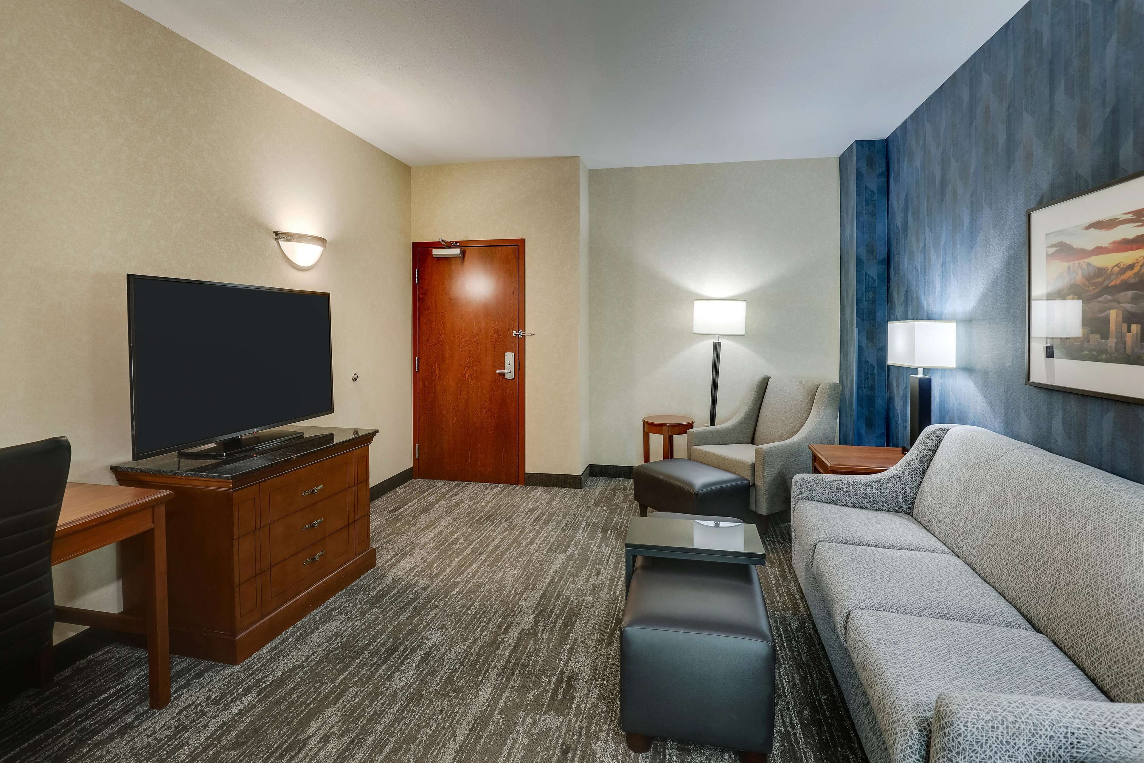 Habitación de hotel con televisor de pantalla plana, escritorio de madera, sofá de cuero y una pequeña mesa.