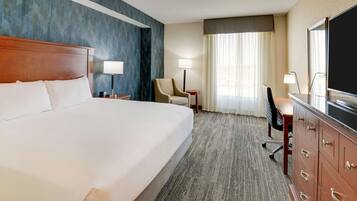 Een hotelkamer met een groot bed, een bureau met stoel, een televisie en een raam met gordijnen.