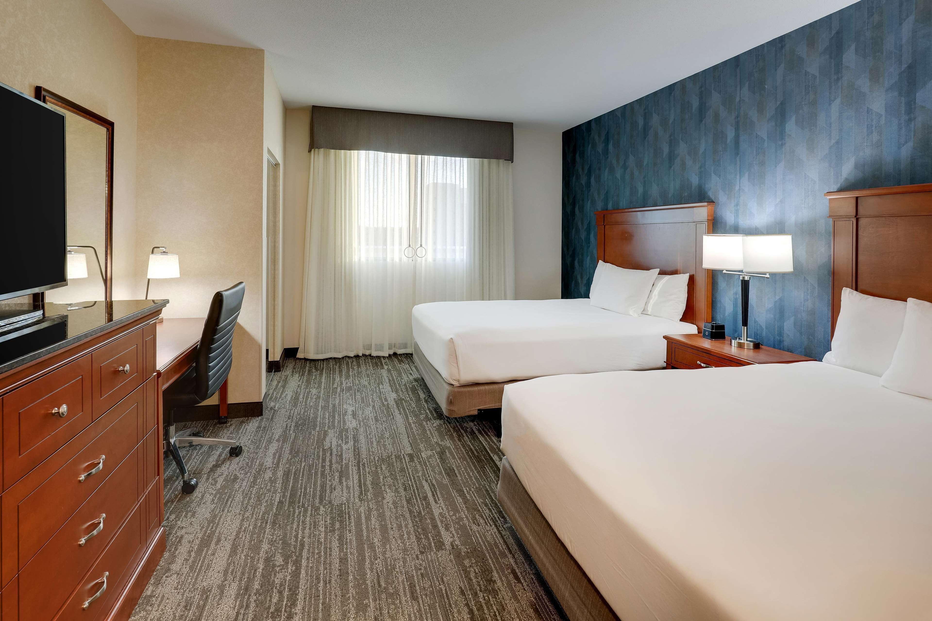 A hotel room with two beds, a desk with a chair, a TV, and a lamp.