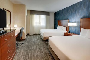 A hotel room with two beds, a desk with a chair, a TV, and a lamp.