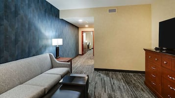 A hotel room with a sofa, a small table, a TV, and a wooden cabinet.