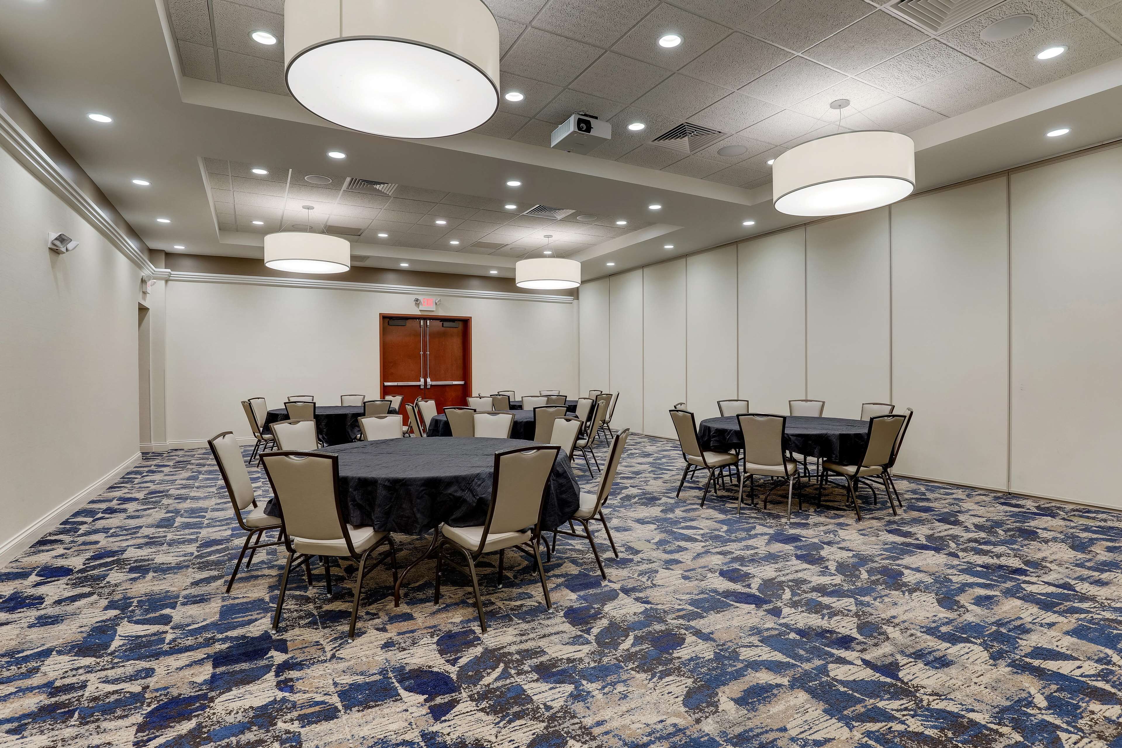 A conference room with round tables and chairs, a patterned carpet, and recessed ceiling lighting.