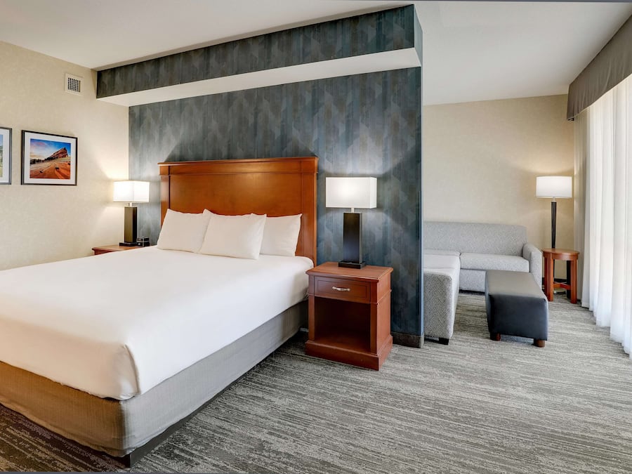 A hotel room with a large bed, two bedside tables with lamps, a sofa, a small ottoman, and a chair.