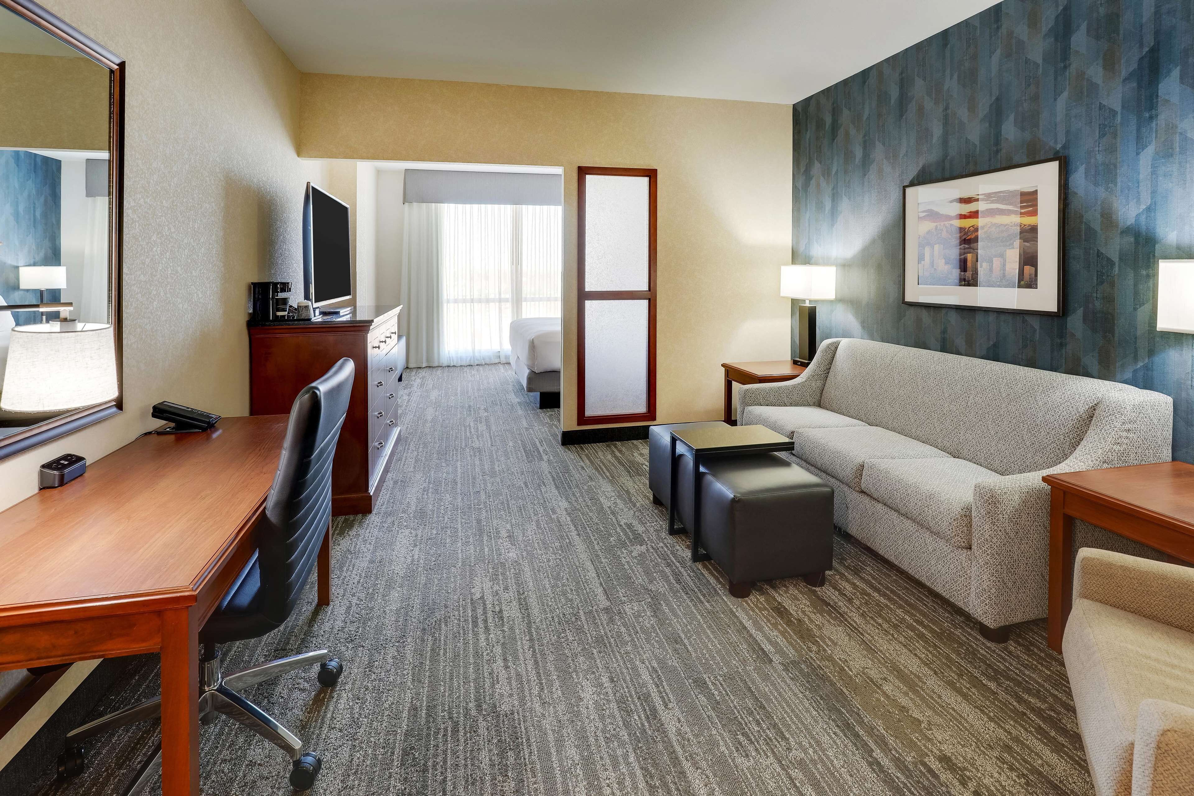 A hotel room with a wooden desk, a sofa, a coffee table, a TV, a bed, and a large mirror.