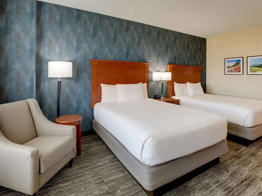 A hotel room with two beds, a sofa, and a lamp.