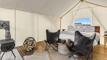 Een tent met een bed, twee zwarte stoelen, een houtkachel en uitzicht op de lucht.
