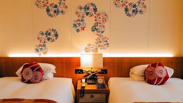 Una habitación de hotel con dos camas, una mesita de noche con lámpara y decoración floral en la pared.