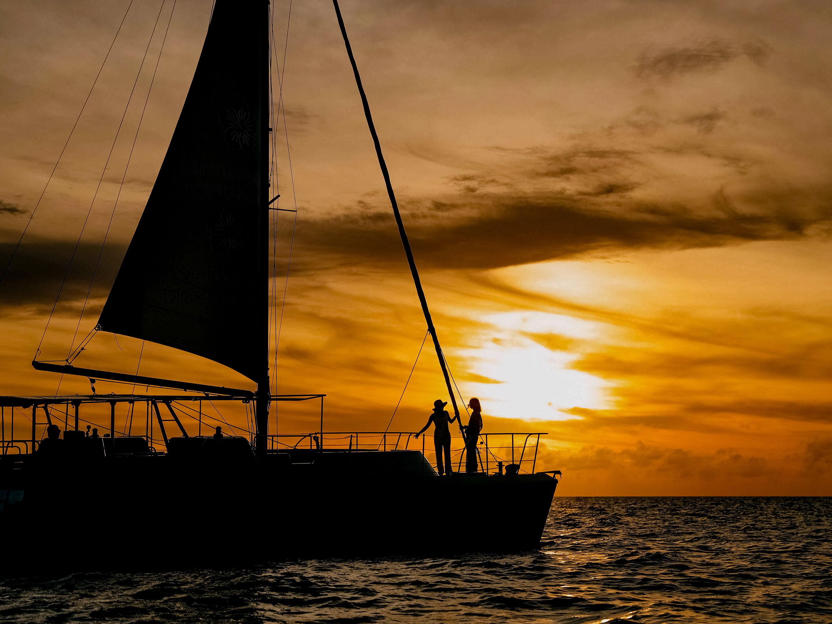 A sailboat with two people on deck during sunset.