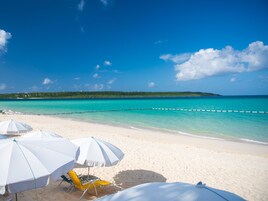A beach with white umbrellas and a yellow chair, a clear blue sky, and turquoise water.