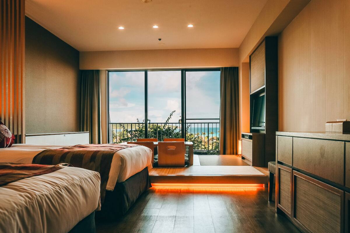 Habitación de hotel con dos camas, un televisor, un balcón con vista a la playa y un escritorio con silla.